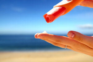 Etwas Sonnenmilch wird auf die Hand einer Frau, die an einem Strand ist, aufgetragen.